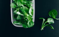 Close-up of fresh green salad leaves in a plastic container on a black background.